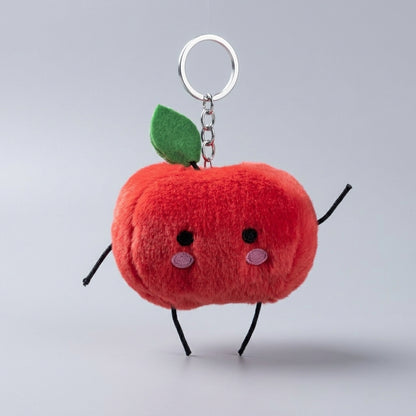 A red junimo keychain with a green leaf, embroidered eyes and cheeks, and black wire arms and legs, attached to a silver metal key ring on a light gray background.