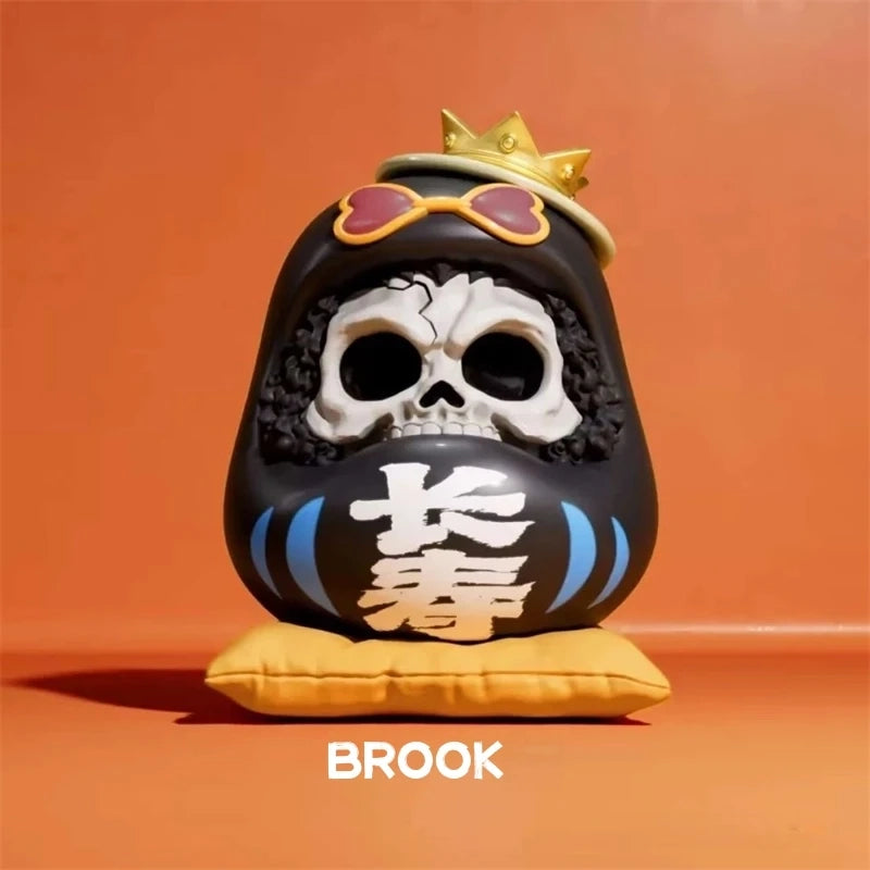 One Piece Daruma figurine of Brook, featuring a skull face, curly hair, crown, and heart-shaped sunglasses on a yellow cushion.
