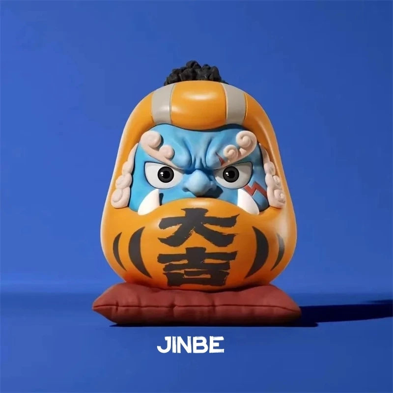 One Piece Daruma figurine of Jinbe, featuring blue skin, sharp teeth, and a fierce expression on a red cushion against a blue background.