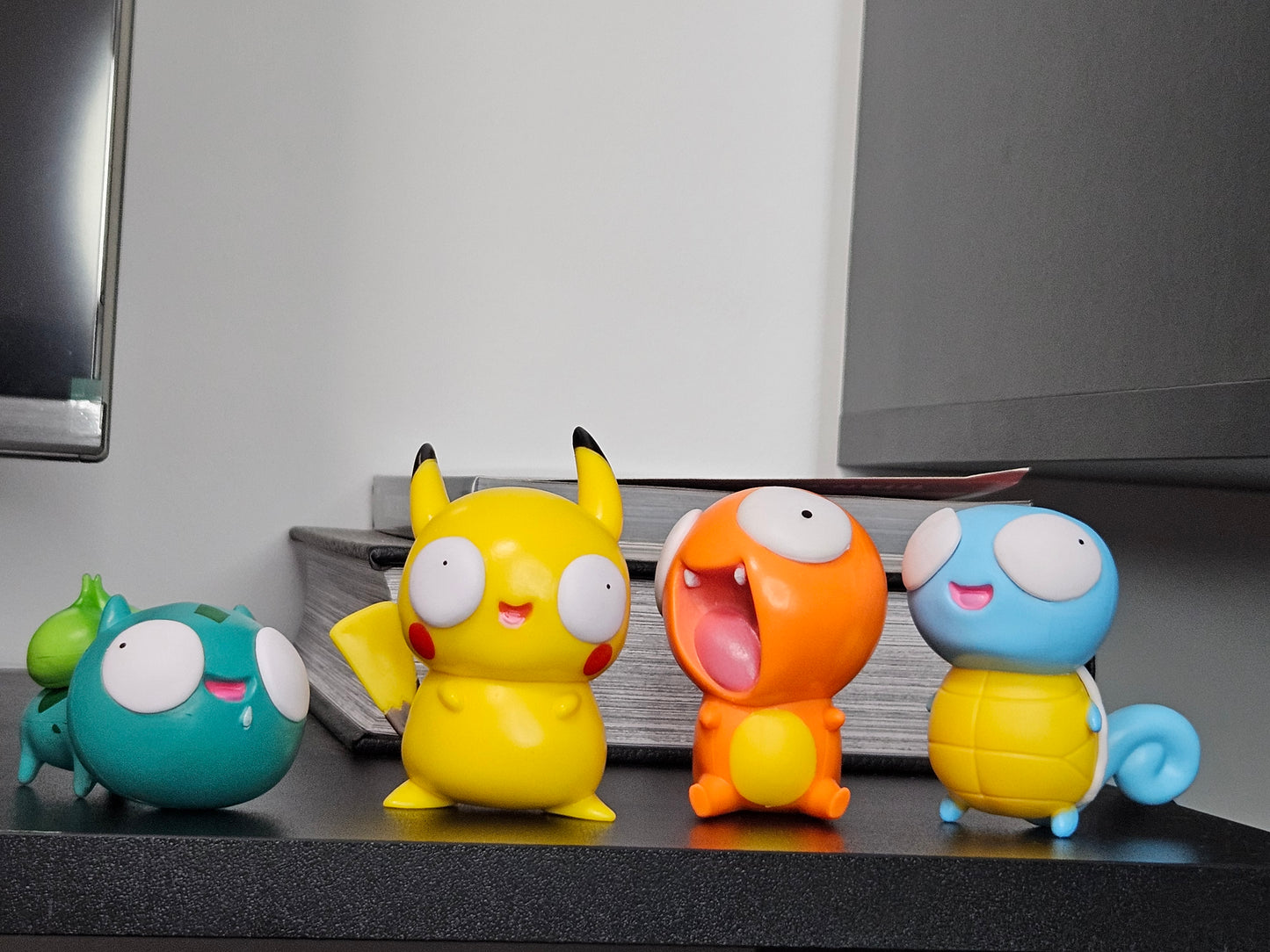 A group of funny Pokémon figurines featuring Bulbasaur, Pikachu, Charmander, and Squirtle with silly, derpy expressions displayed together on a shelf for a quirky and playful collection centerpiece