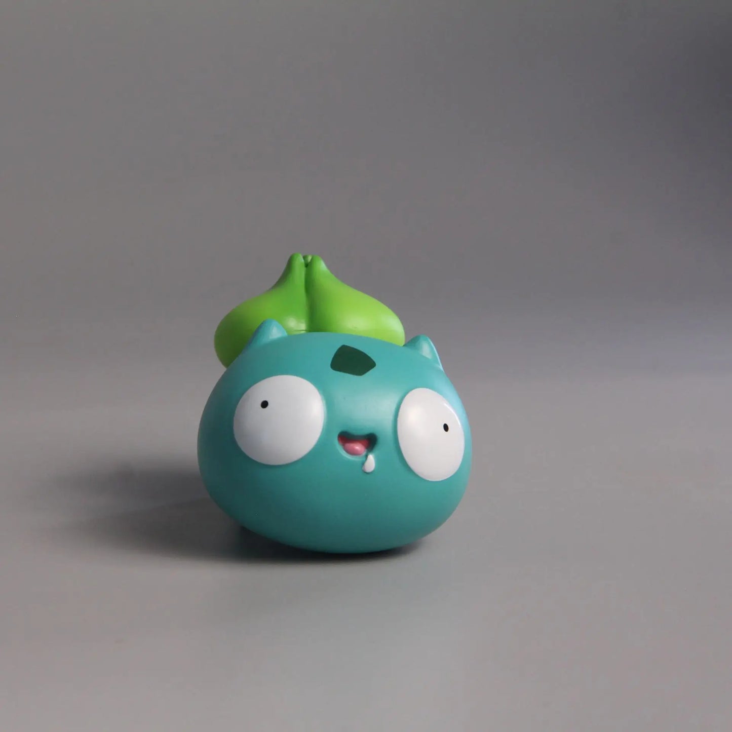 Funny Bulbasaur figurine with a round, derpy face, wide eyes, and a playful smile, showcasing a humorous take on the beloved Pokémon character.