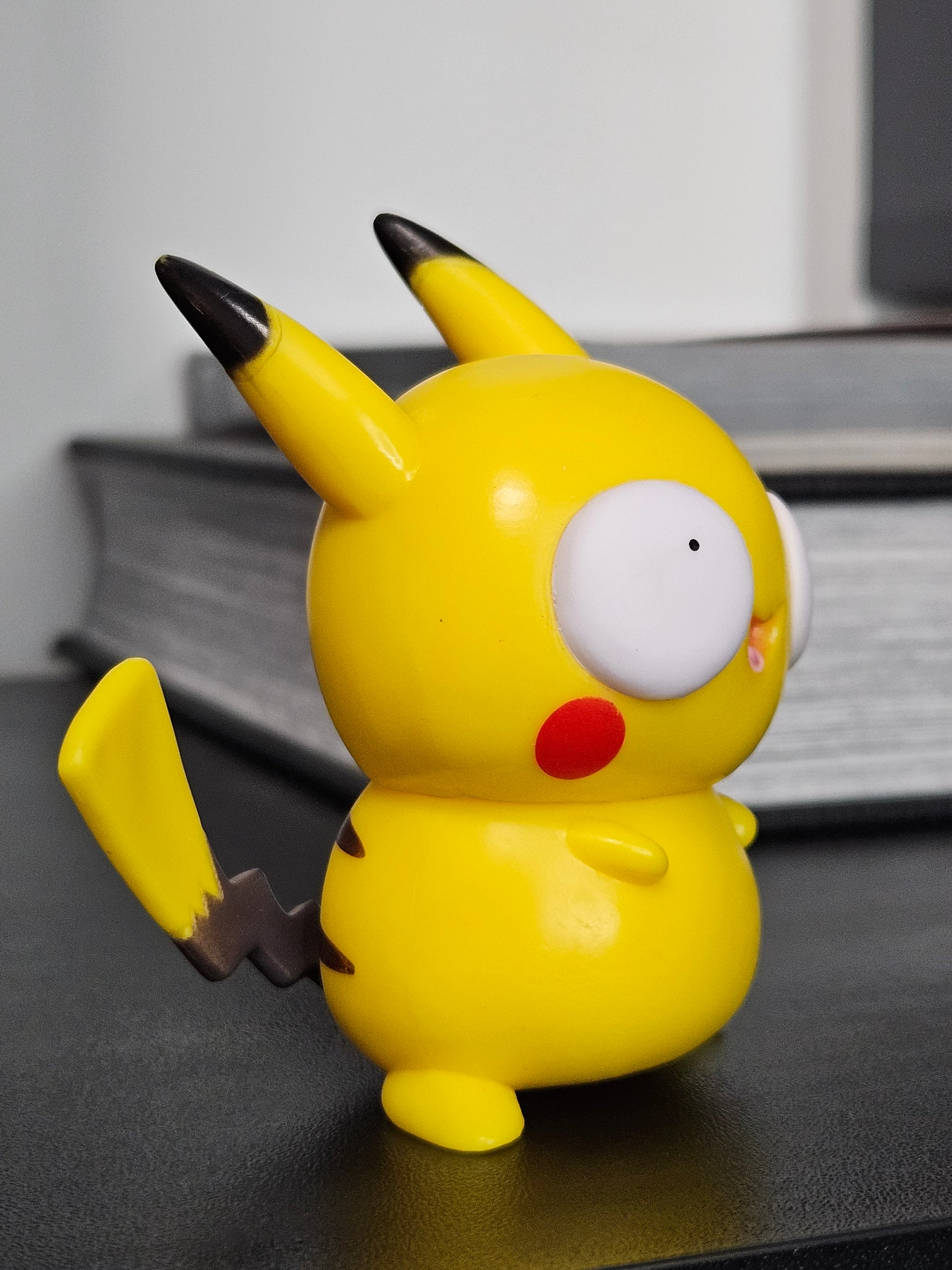 Side view of a funny Pikachu figurine with derpy wide eyes, red cheeks, and its signature lightning bolt tail, showcasing a playful and quirky take on the beloved Pokémon character