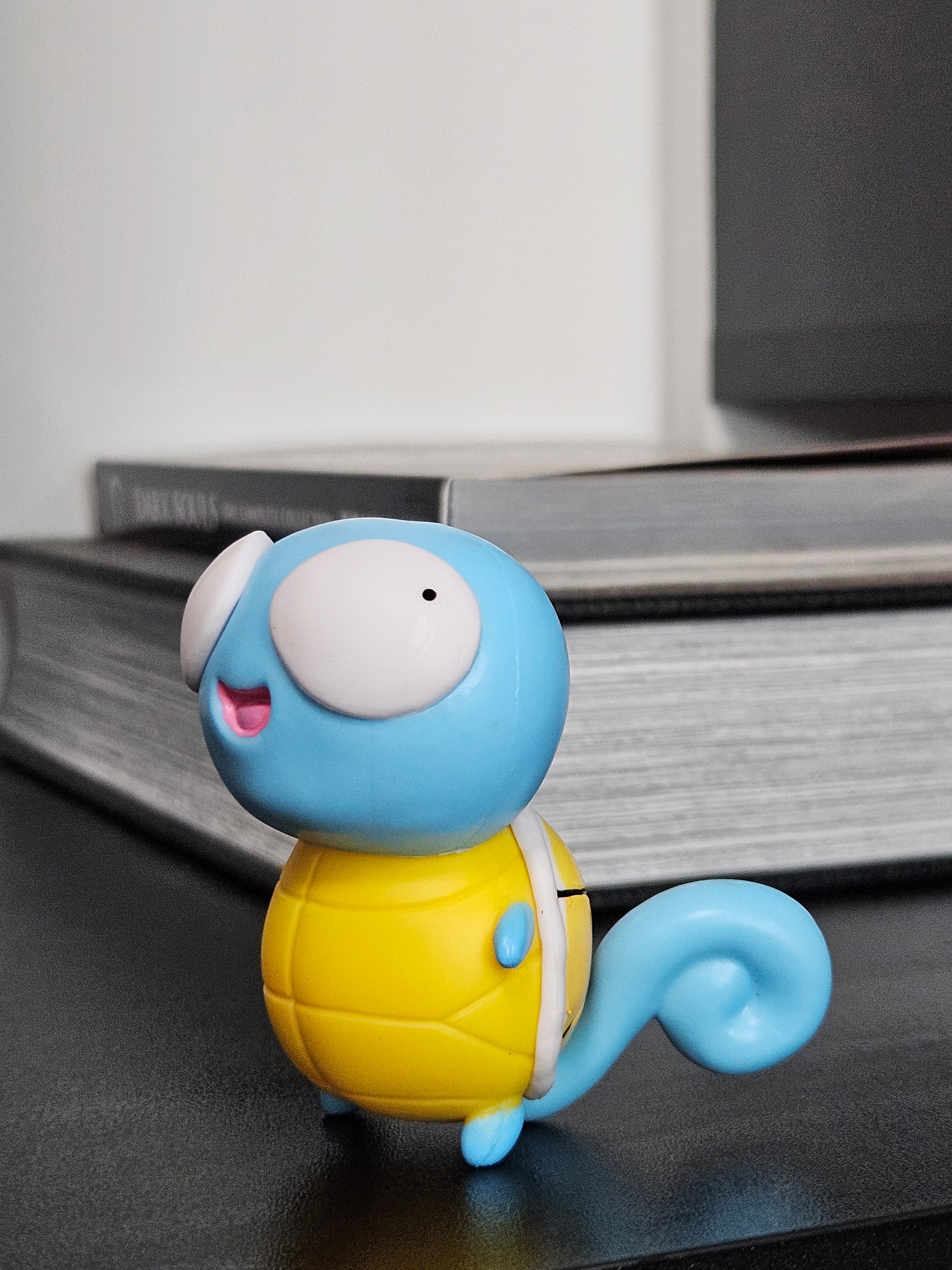 Side view of a funny Squirtle figurine featuring derpy wide eyes, a cheerful smile, and a curly blue tail, showcasing its playful and quirky design for fans and collectors