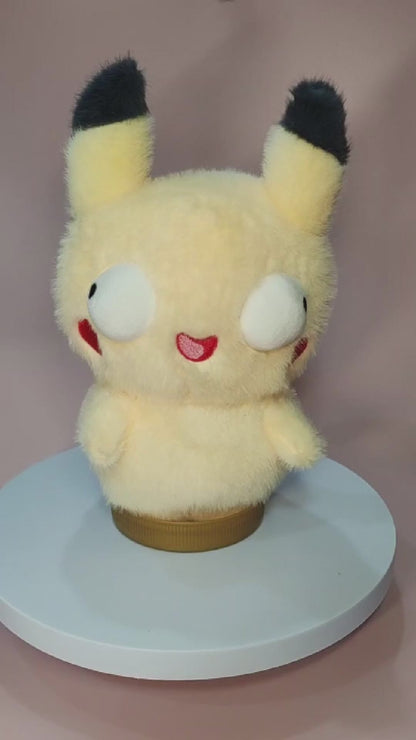 Alt text: Silly "Pokederp" Pikachu plushie with a fuzzy yellow body, oversized round eyes looking in different directions, and a tiny, goofy open-mouthed smile. The plush has black-tipped ears, red cheek patches, and stubby arms. It sits on a rotating display stand against a pastel pink background.